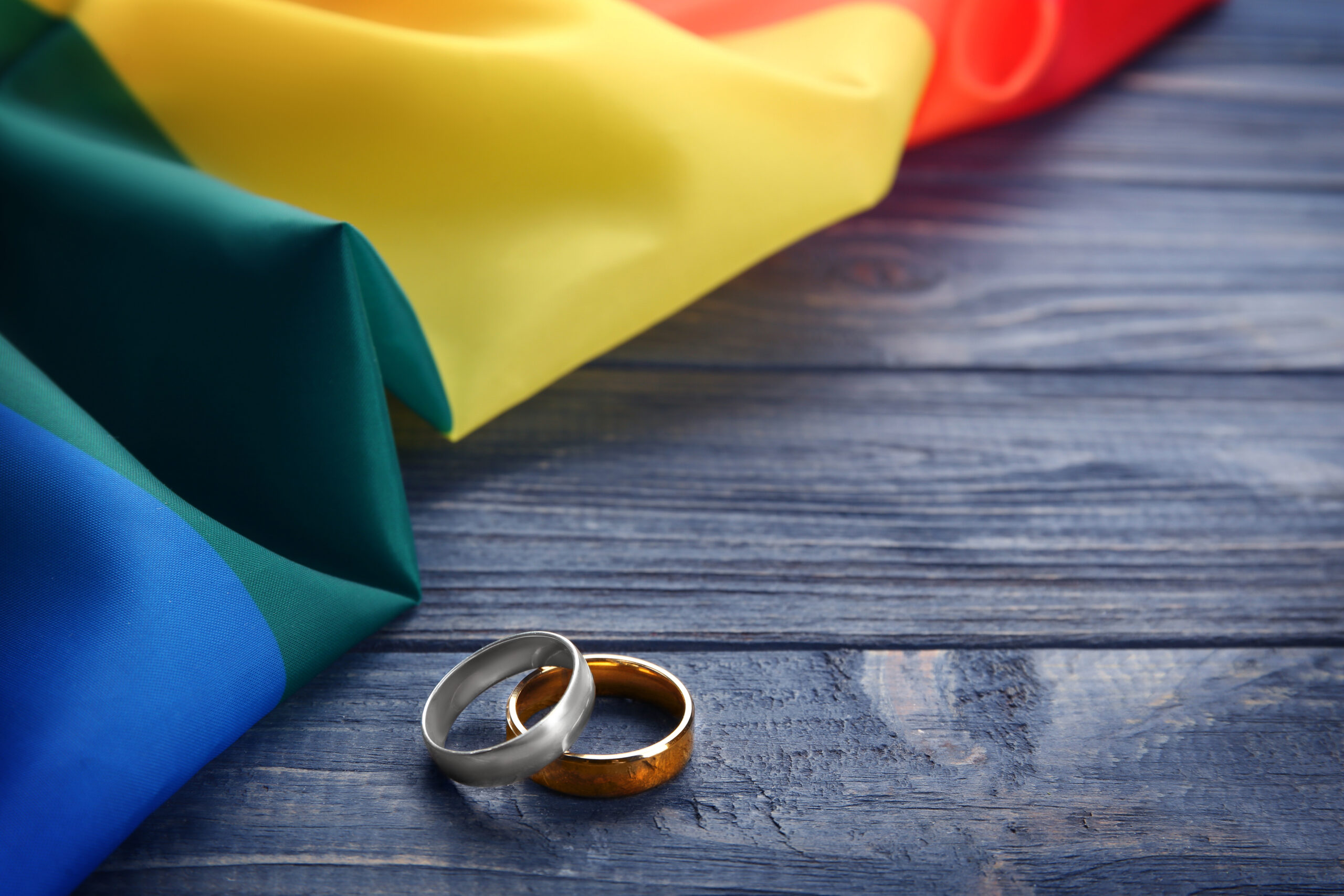 Two,Wedding,Rings,And,Rainbow,Gay,Flag,On,Wooden,Background