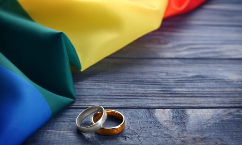 Two,Wedding,Rings,And,Rainbow,Gay,Flag,On,Wooden,Background